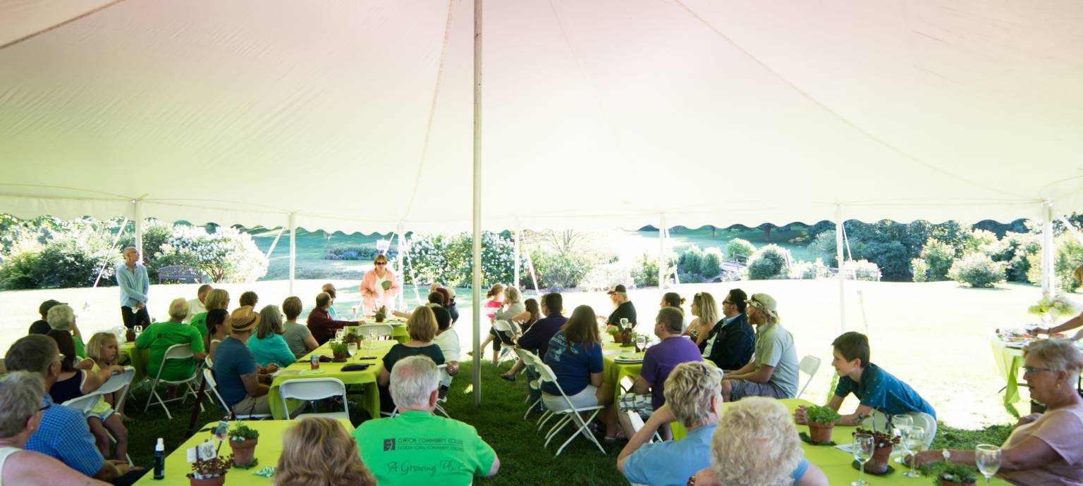 Group of trip goers sitting under a tent at tables for an event in Clinton Iowa